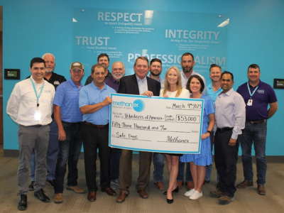 group of employees smiling and holding a check for Volunteers of America from Methanex