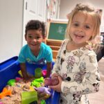 two kids smiling into camera while playing with toys