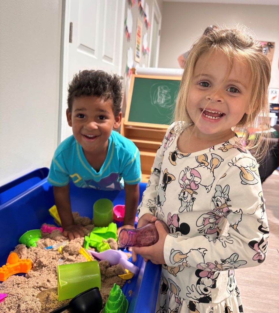 two kids smiling into camera while playing with toys